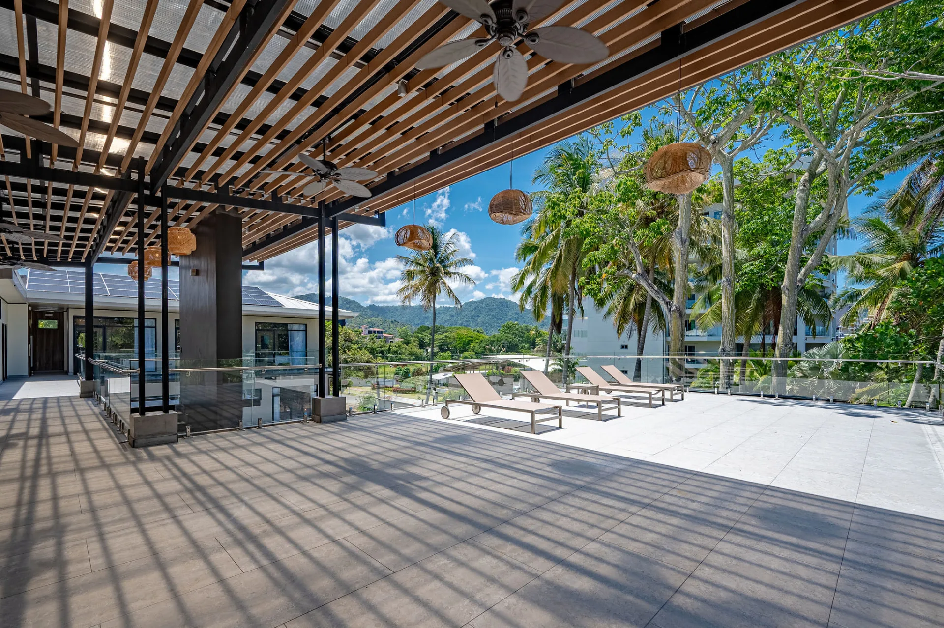 Covered open-air terrace with slatted pergola and loungers looking out to the palms and mountains